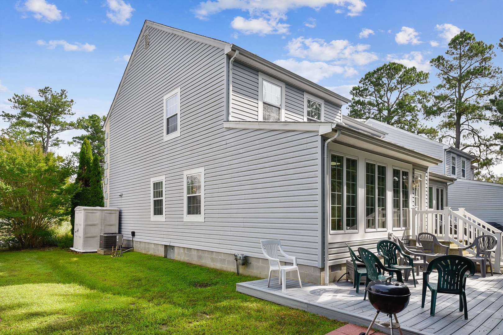 A spacious two-story home with a bright deck and BBQ area, surrounded by trees in a quiet neighborhood—perfect for relaxing and dining outdoors.