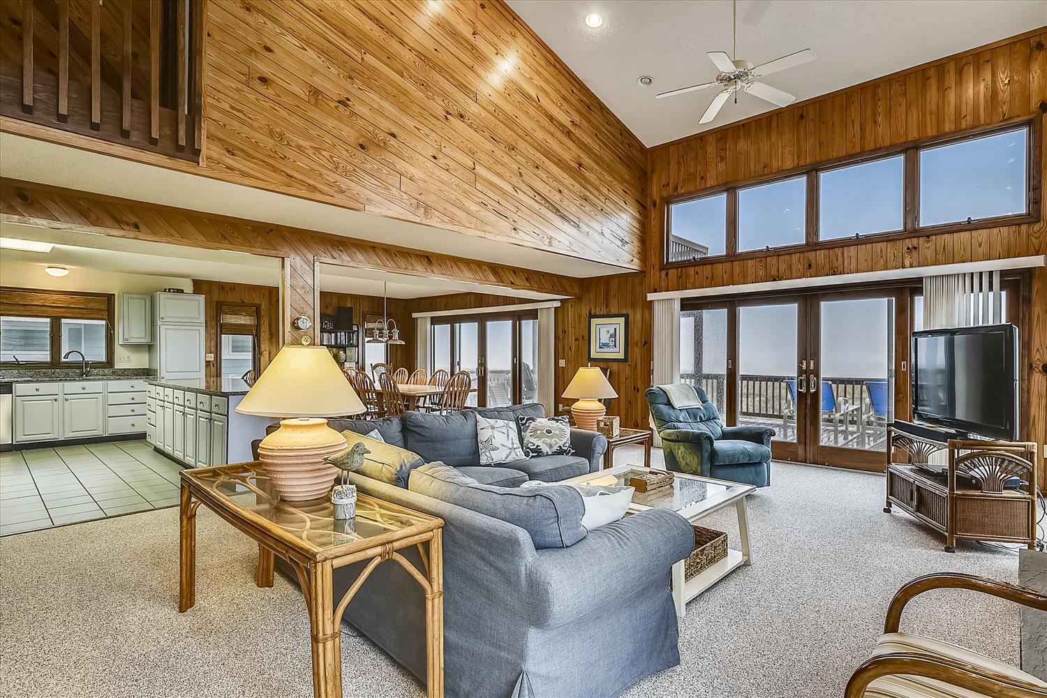 Spacious coastal retreat with warm wood-paneled walls, vaulted ceilings, and expansive windows framing ocean views. Open layout with plush seating, full kitchen, and private balcony with sea breeze.