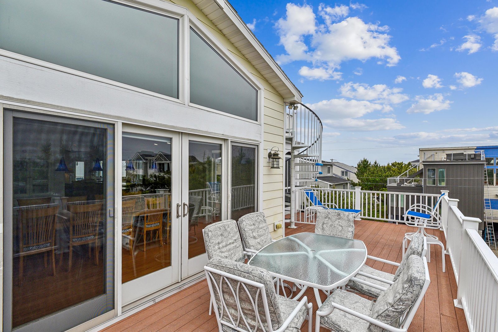 A spacious second-story deck offering your private outdoor escape, complete with dining space and spiral stair access, framed by open skies and a peaceful neighborhood setting.