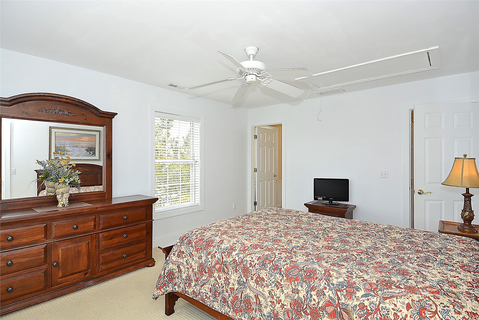 Rest easy in your spacious bedroom with classic wooden furnishings, a ceiling fan for comfort, and entertainment right at your fingertips with a flat-screen TV.
