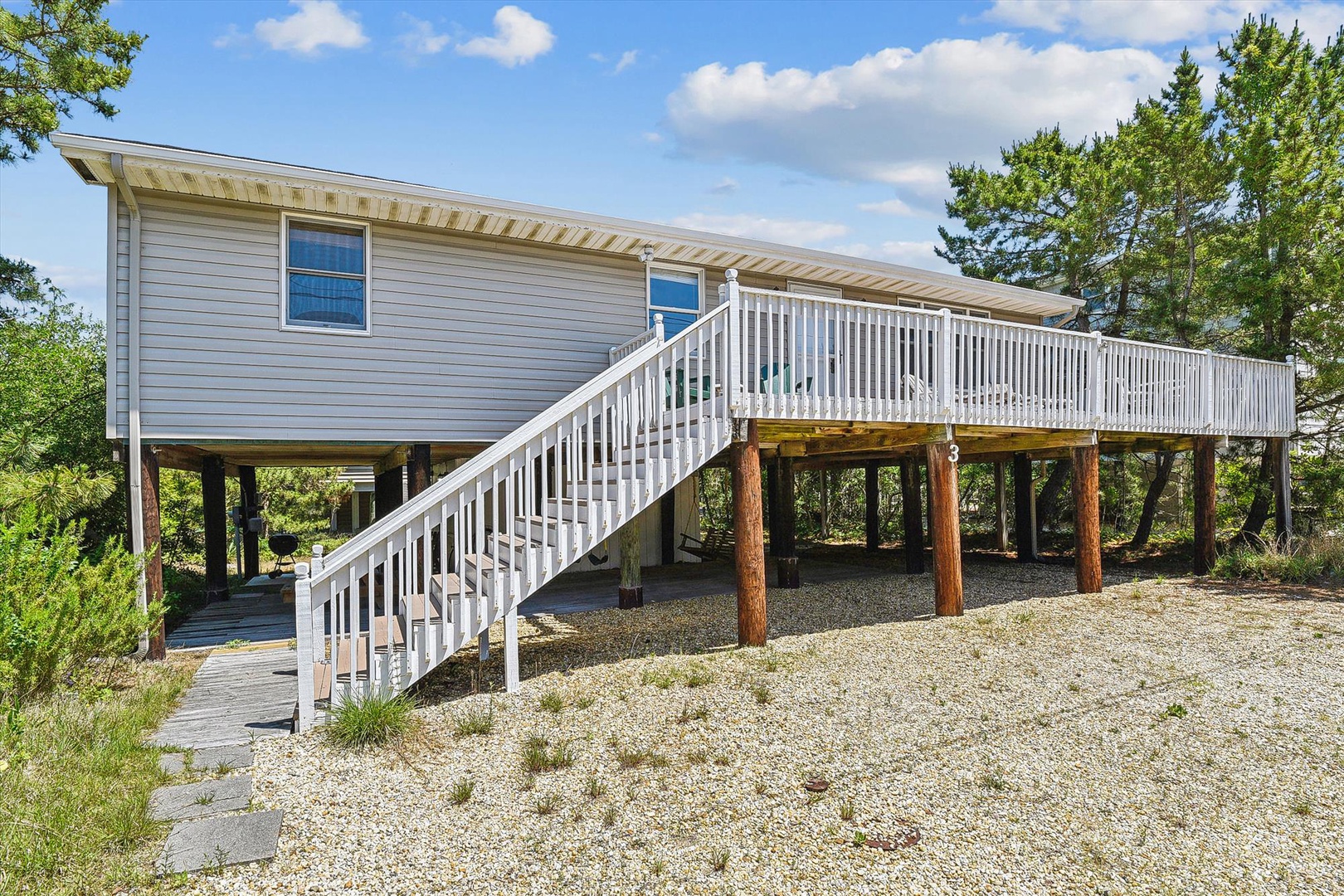 Coastal vacation home elevated on stilts with spacious deck, surrounded by lush greenery and nestled in a peaceful natural setting.