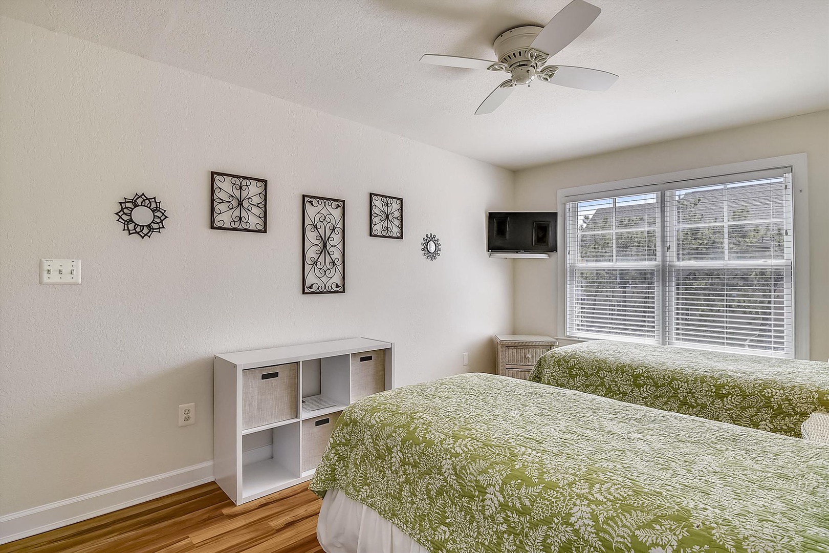 Unwind in your peaceful retreat featuring twin beds with soft green linens, decorative wall art, and natural light streaming in.