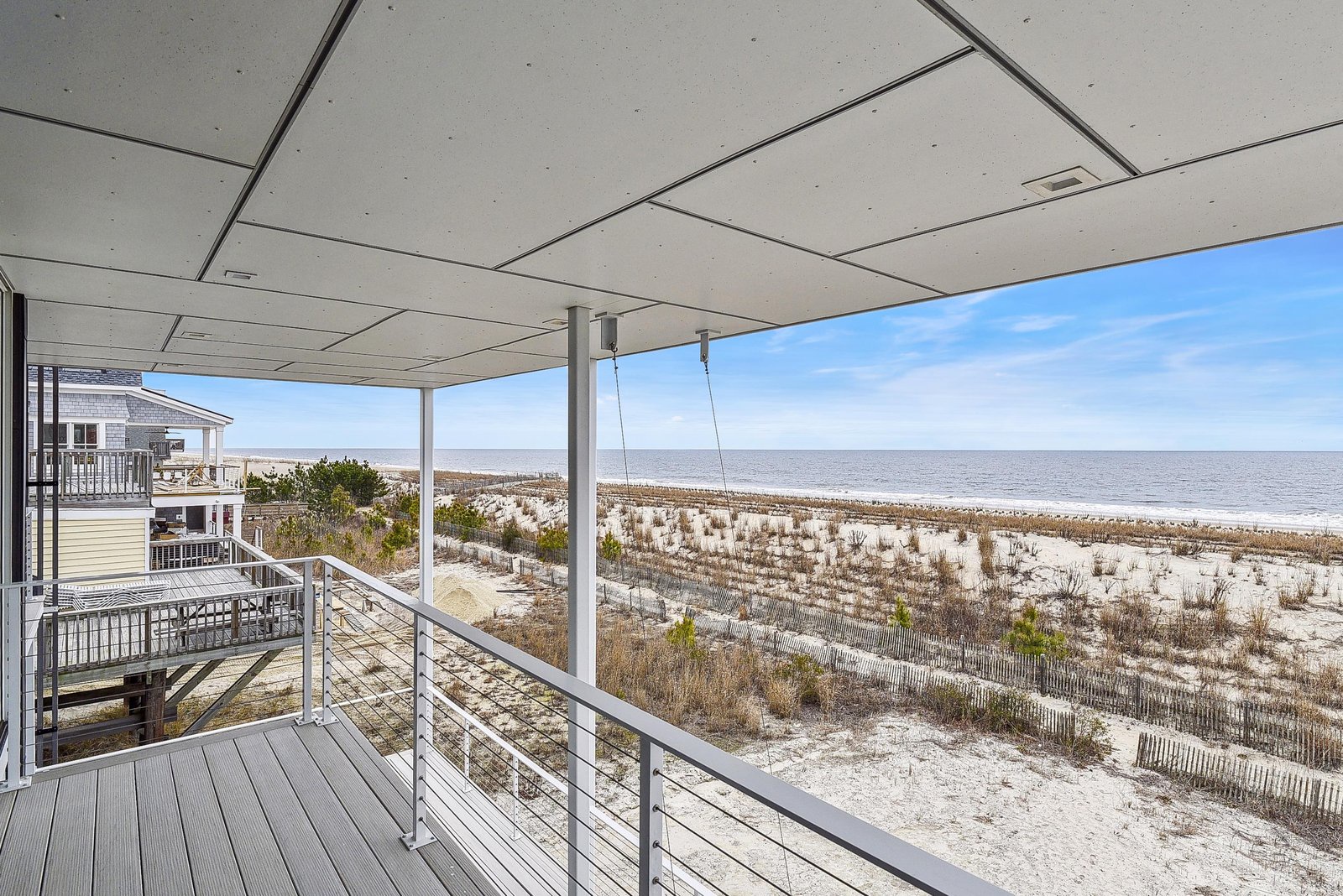 A covered deck just steps from the sandy shoreline, with protective dunes and the ocean stretching toward the horizon.