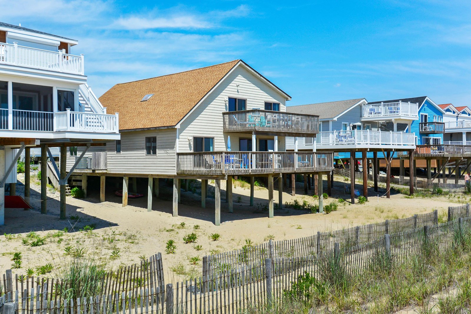 Beachfront vacation homes elevated on stilts line the sandy shore, offering direct access to coastal dunes and ocean breezes in a charming seaside neighborhood.