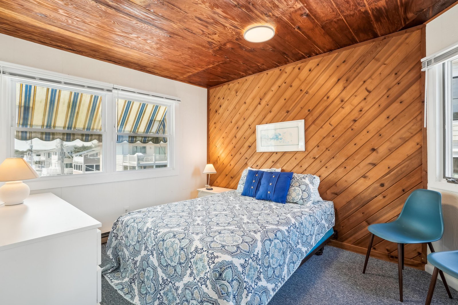 Your cozy bedroom features a stunning diagonal wood accent wall and warm wood plank ceiling. Sink into the plush bed and enjoy the coastal charm through striped awning windows.