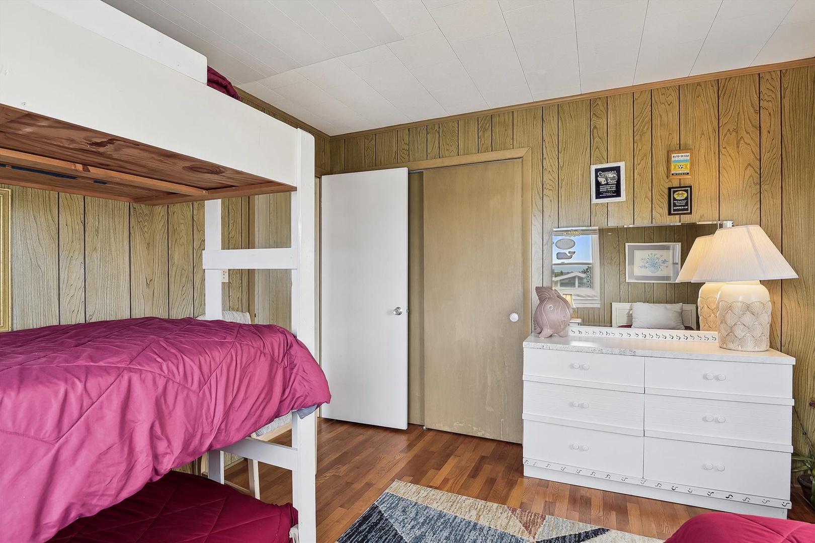 Your cozy bedroom combines rustic wood-paneled charm with thoughtful touches—a bunk setup for flexible sleeping, a bright lamp, and framed memories that make this space feel like home.