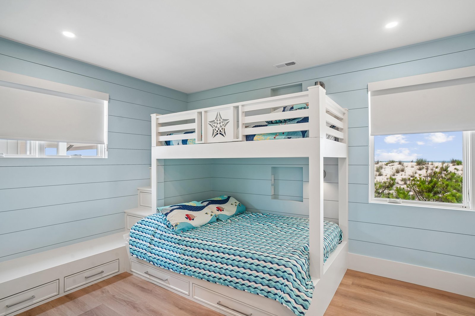 Drift off to the sound of distant waves in this coastal-inspired bedroom with bunk beds and a glimpse of natural dunes and greenery beyond.