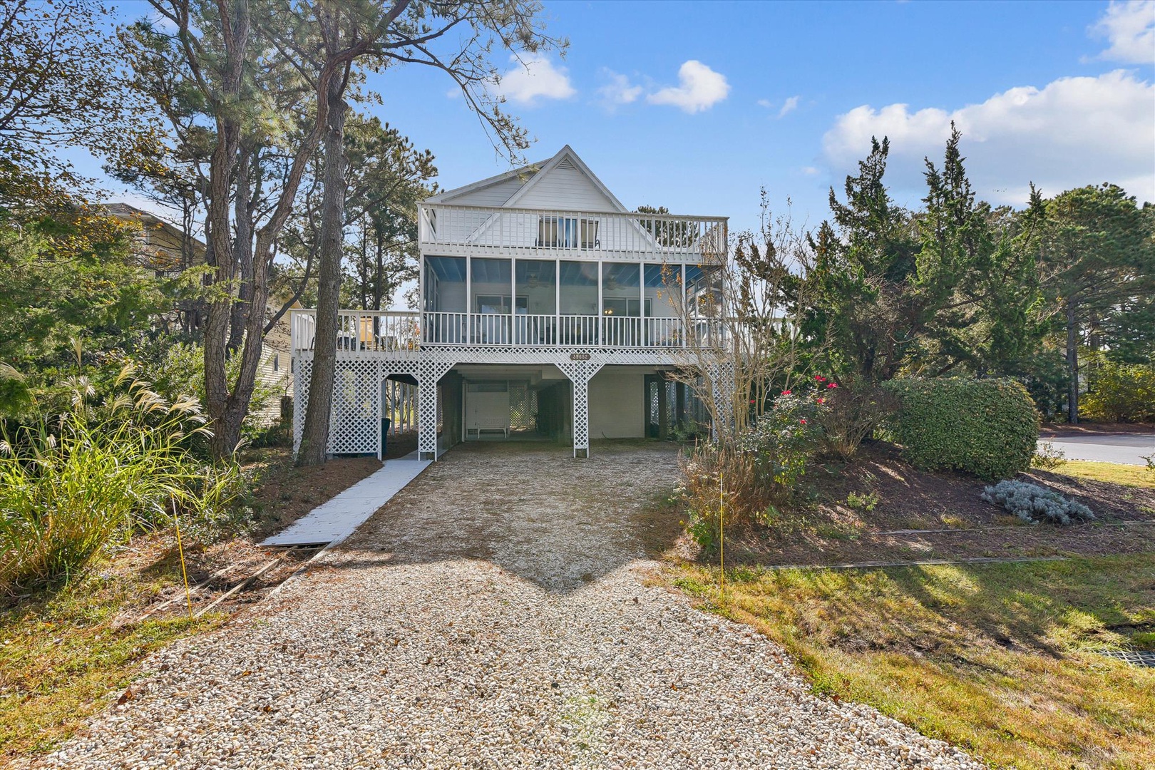 Charming coastal retreat with elevated living spaces and ground-level parking, nestled among mature trees in a peaceful residential setting.