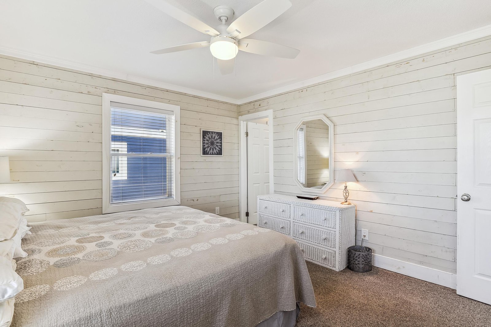 Your coastal retreat awaits in this serene bedroom featuring shiplap walls, a ceiling fan, and a dresser with mirror—everything you need for a restful stay.