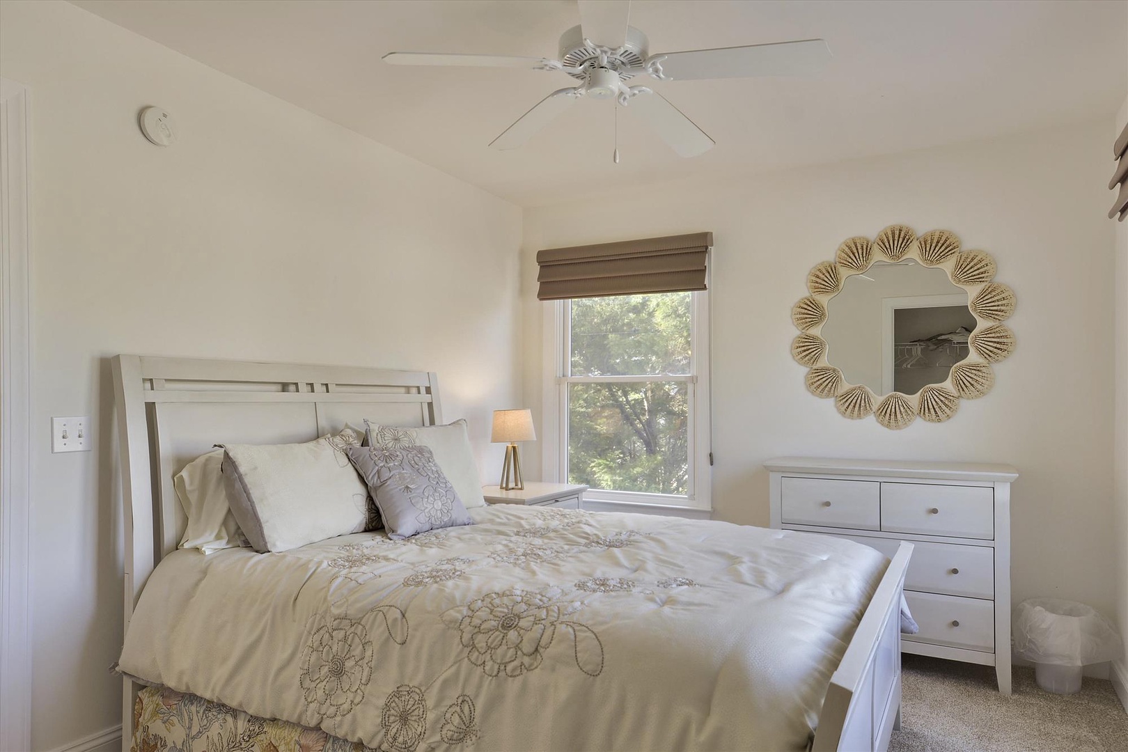 Soft morning light fills your bedroom retreat, where crisp linens and coastal decor invite peaceful sleep. Unwind beneath the ceiling fan with treetop views framing your escape.