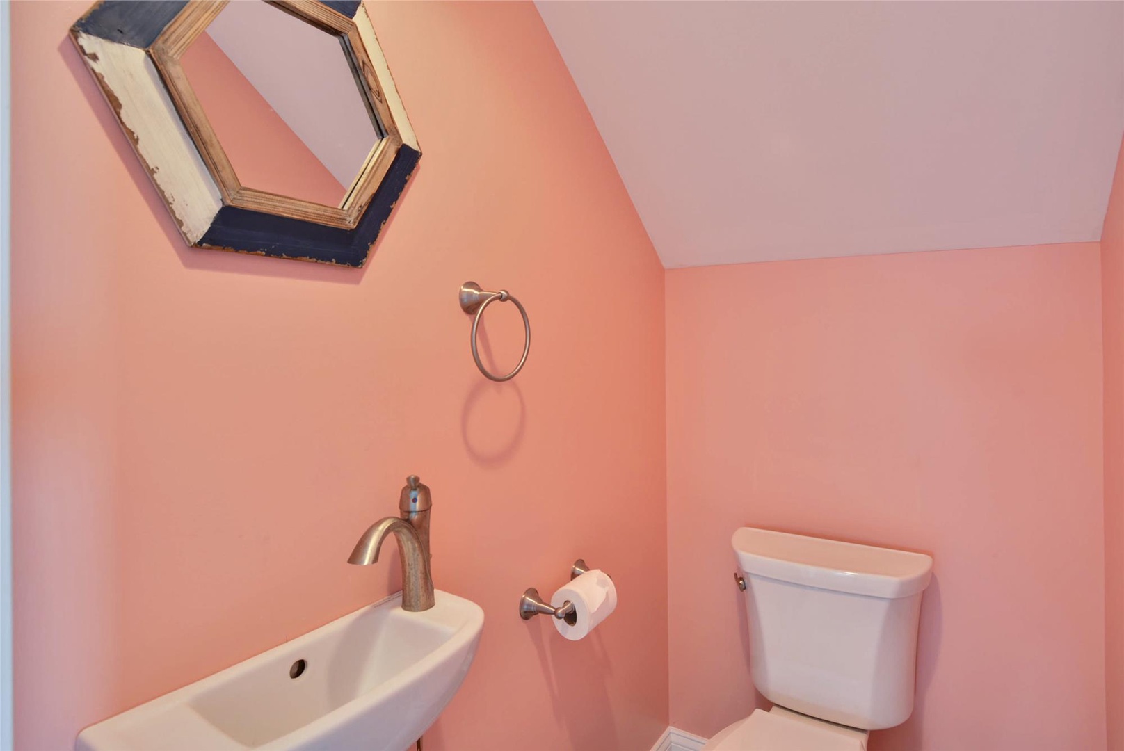 Charming powder room with soft pink walls, skylight above, and compact fixtures perfect for guests—simple, bright, and welcoming.