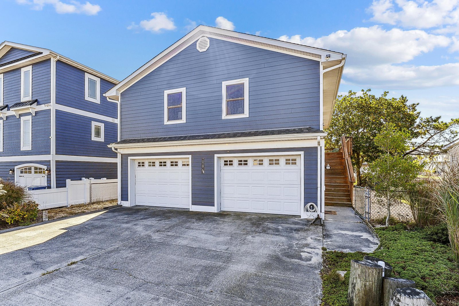 This charming blue-sided property features a spacious two-car garage and ample driveway parking, nestled in a peaceful neighborhood setting with mature trees.