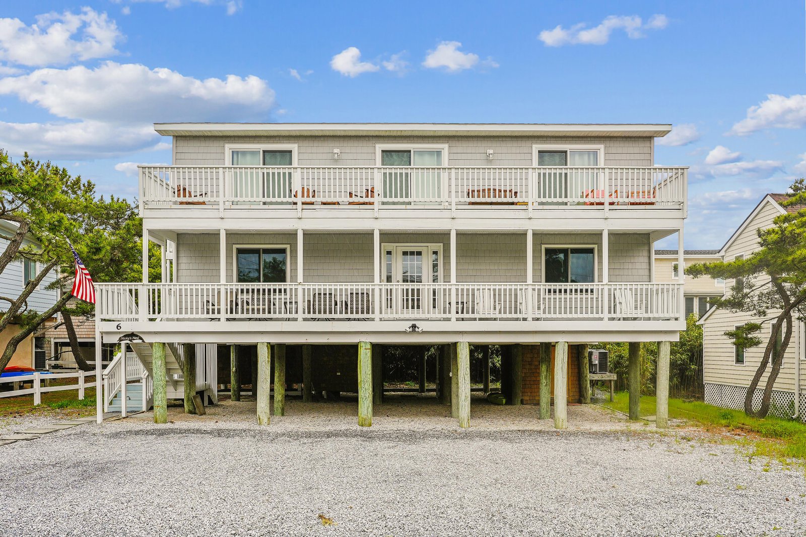 A spacious beach house featuring three levels, expansive balconies with outdoor lounging, and generous parking space beneath elevated construction—ideal for a coastal getaway with family or friends.
