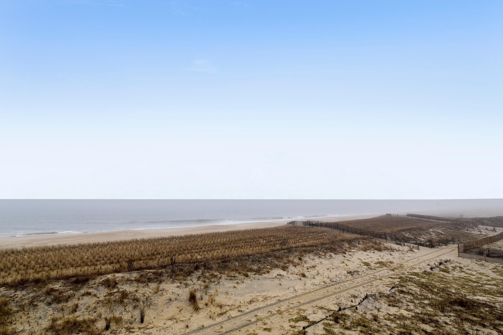 A peaceful coastal property surrounded by natural dunes and sandy paths, with the ocean stretching along the horizon.