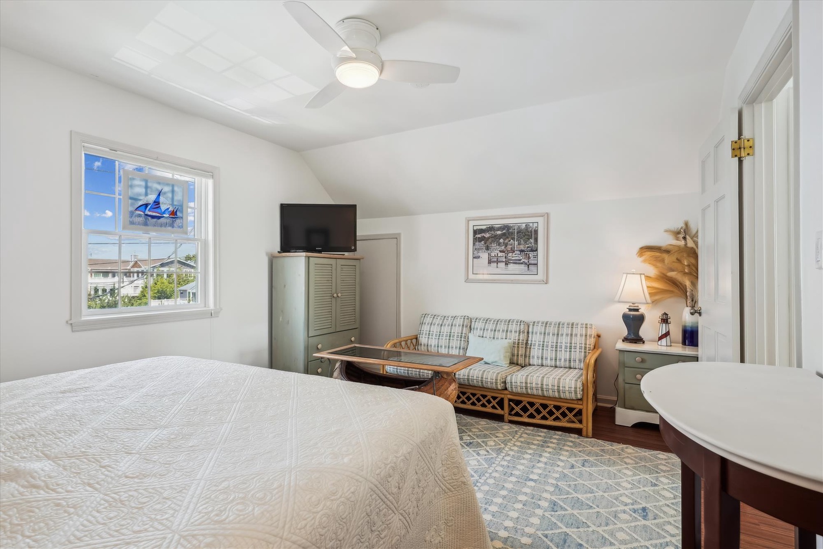 Relax in your cozy bedroom with crisp linens, a ceiling fan overhead, and coastal charm all around. Your private retreat includes a TV, comfy seating area, and gentle breezes from the window—perfect for unwinding after a day at the beach.