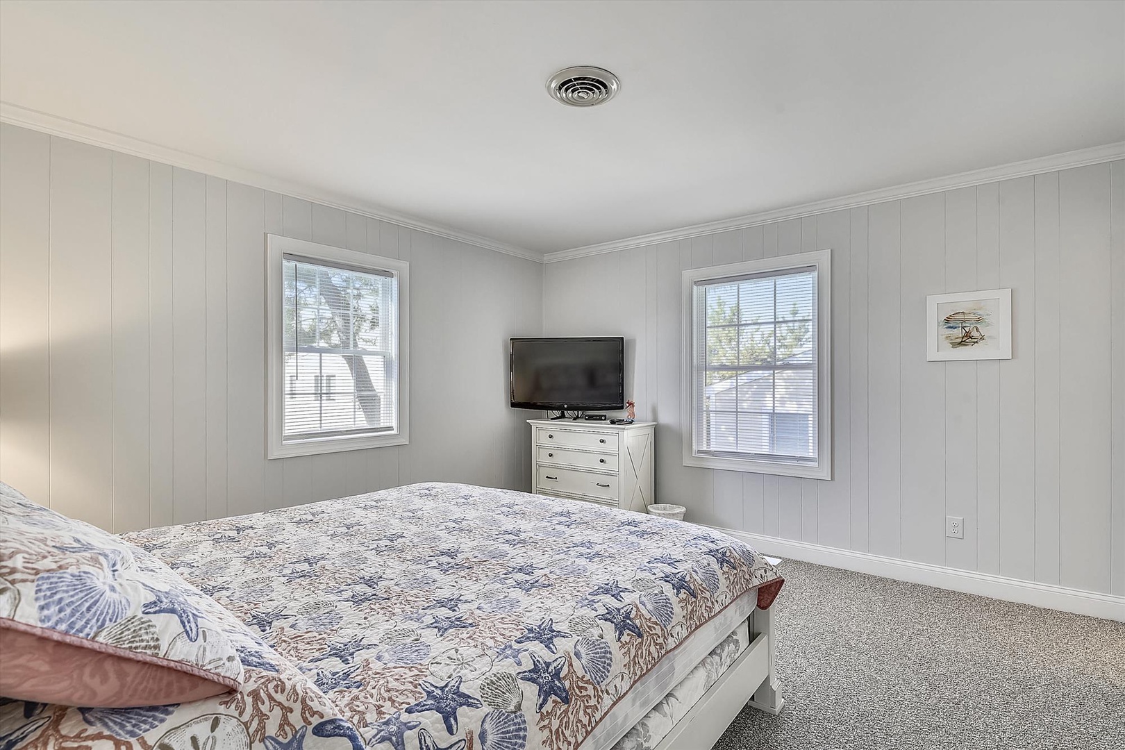 Your serene coastal-themed bedroom features soft white paneling, a cozy bed with seaside linens, and windows framing peaceful outdoor views for restful nights.