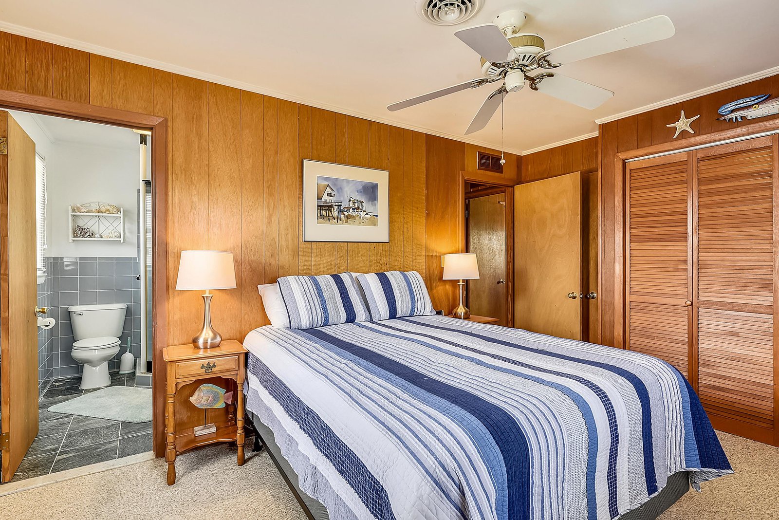 Relax in your cozy bedroom with warm wood paneling, a comfortable bed dressed in nautical stripes, and a ceiling fan to keep you cool.
