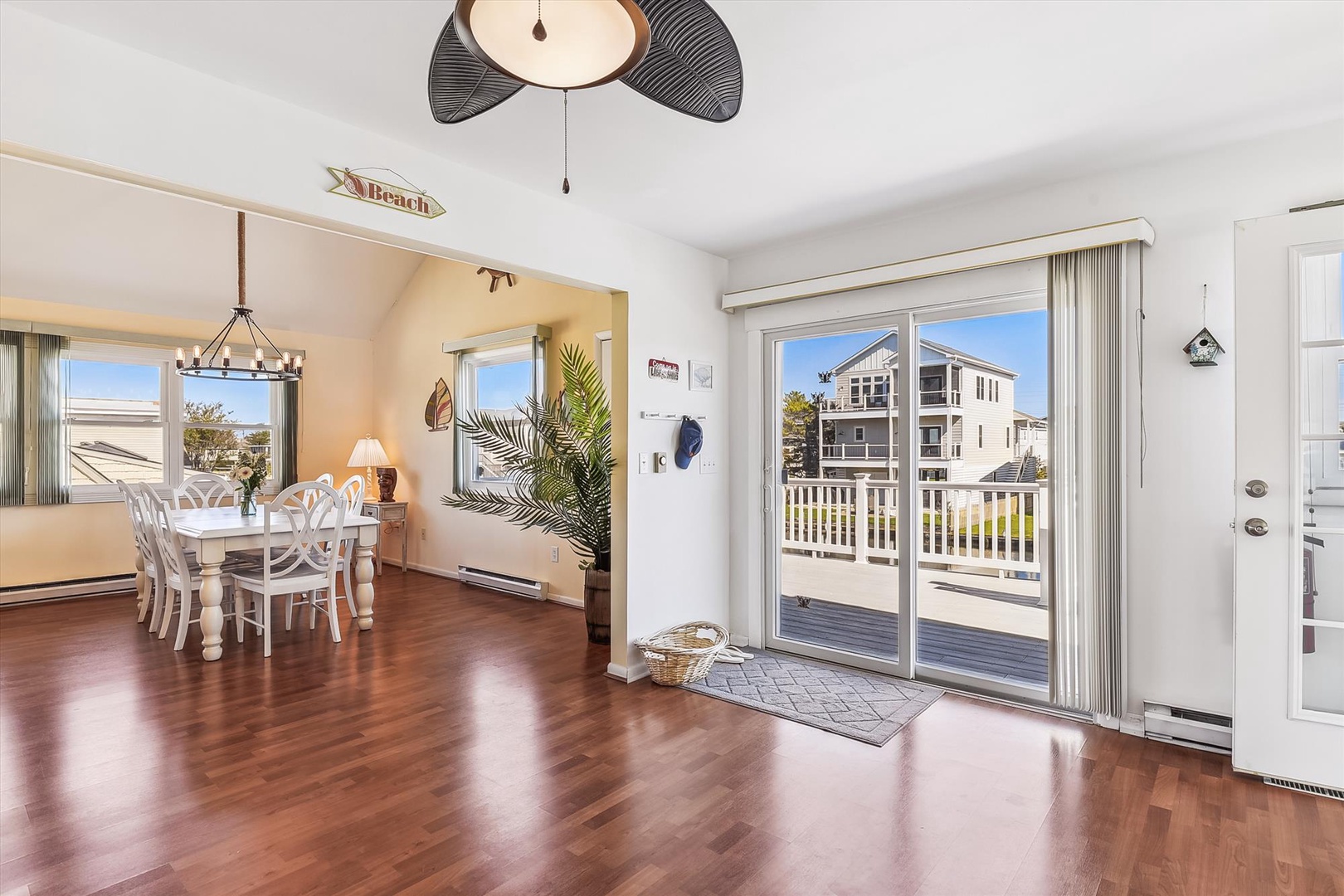 Sunlight pours through large glass doors, illuminating gleaming hardwood floors and your open dining space, where a ceiling fan adds coastal charm and a balcony awaits your morning coffee.