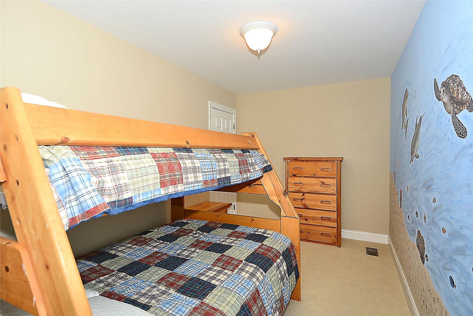 Your kids will love their own cozy bunk room with cheerful plaid bedding, wooden dresser, and charming nature-themed mural perfect for sweet dreams.