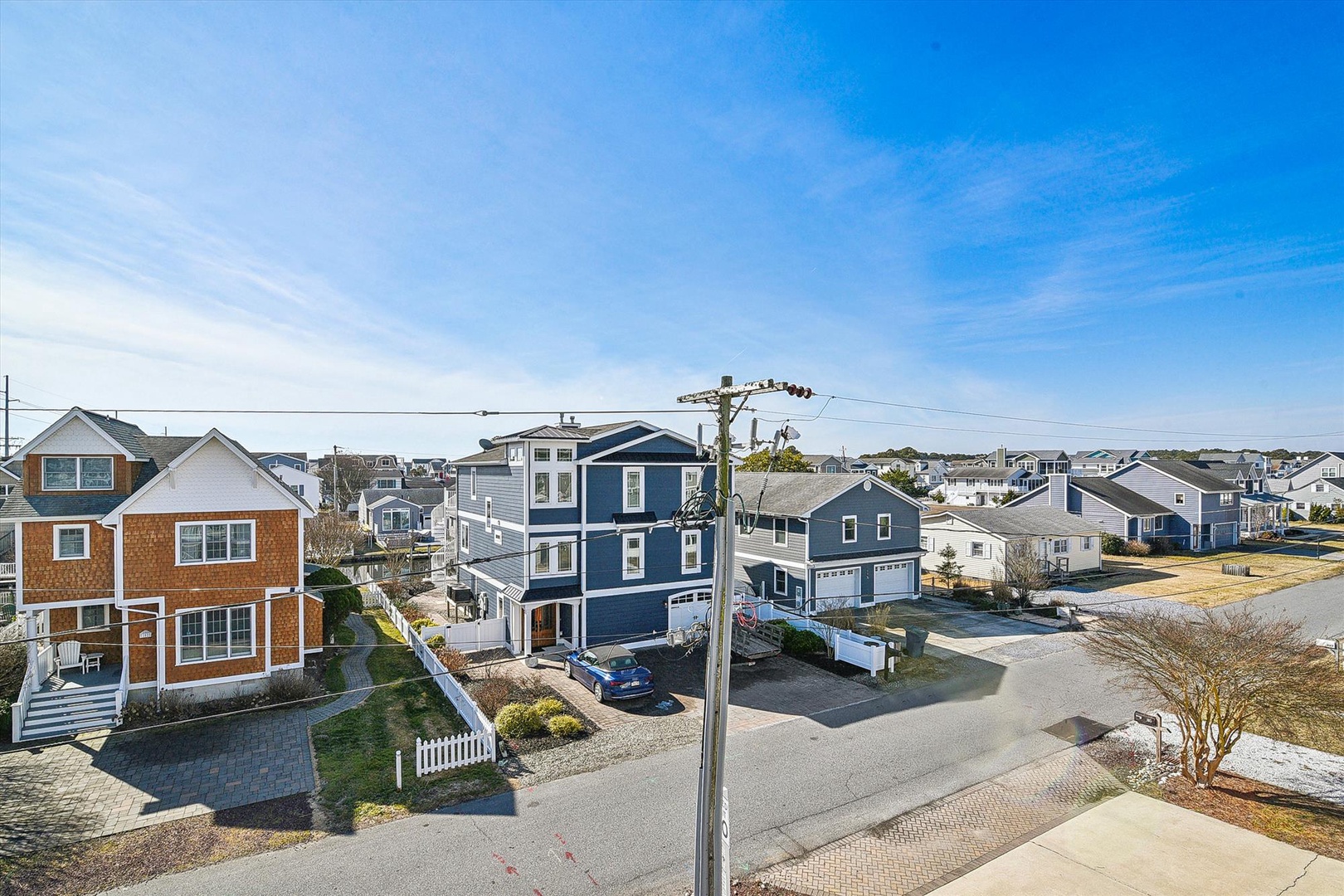 Aerial view of a coastal residential neighborhood featuring diverse beach house architecture under a clear blue sky. The property is located in a peaceful seaside community.