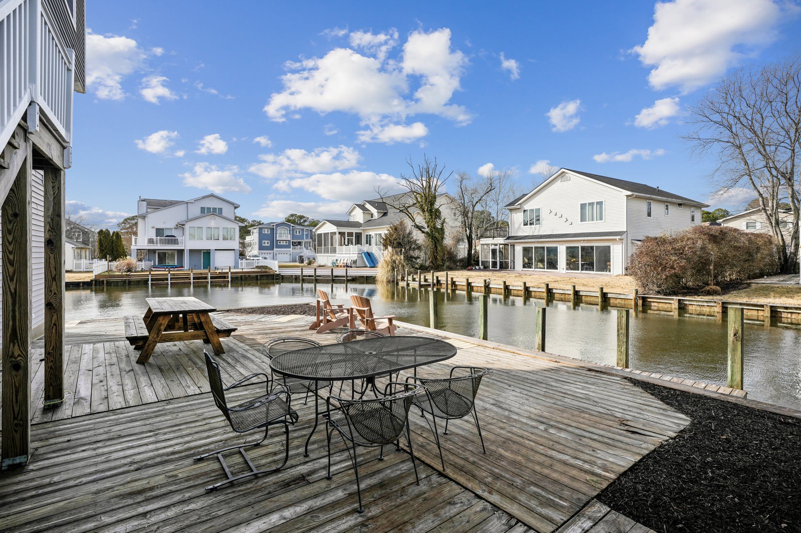 Private waterfront deck with dining table, picnic table, and dock access on peaceful canal surrounded by charming homes.