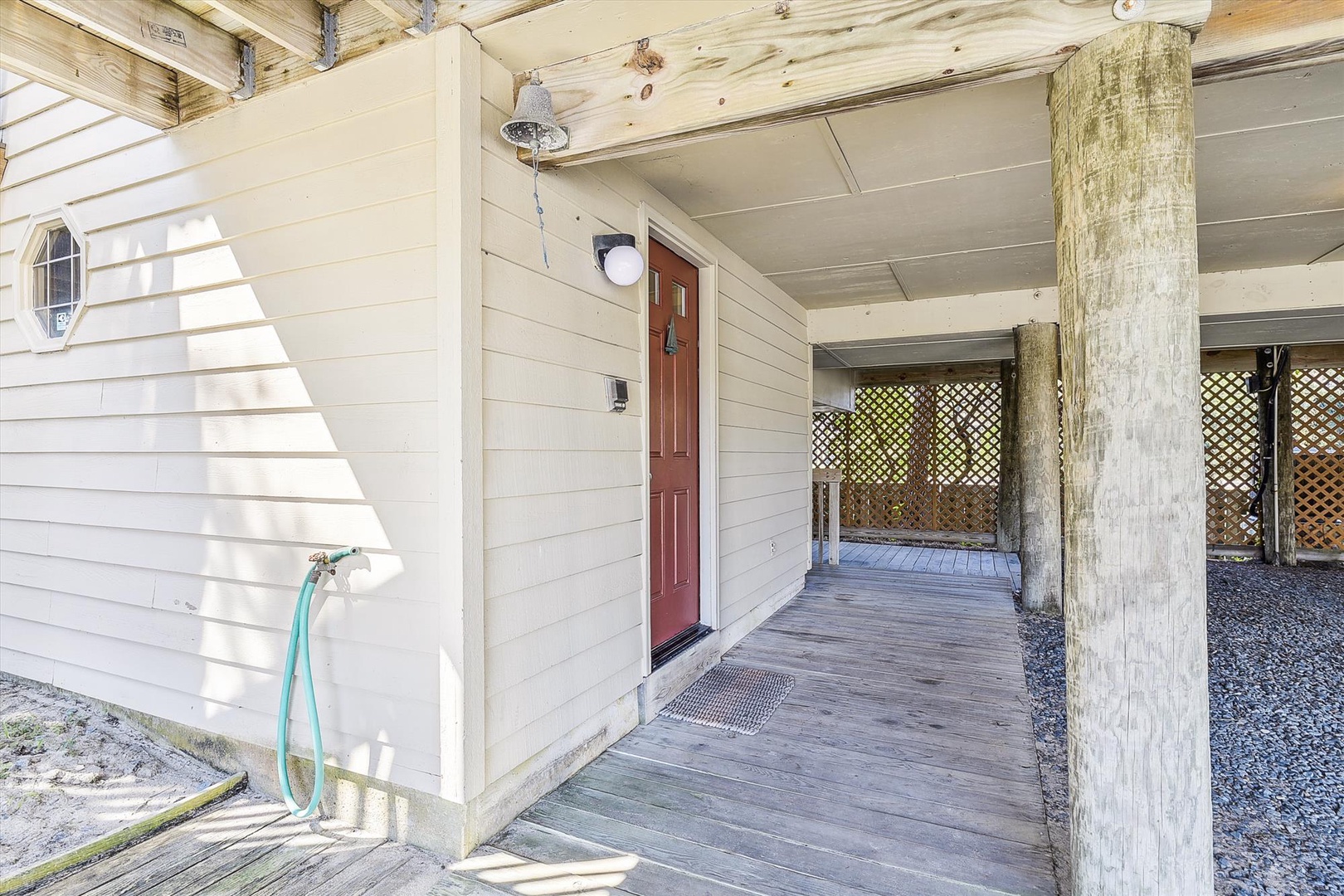 Covered entrance with rustic wood columns and decking, leading to a welcoming red door beneath an elevated coastal cottage.