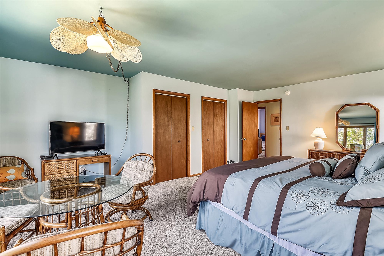 Relax in your spacious room featuring a comfy bed, cozy seating area with TV, and charming rattan furnishings—your perfect retreat after a day of adventure.