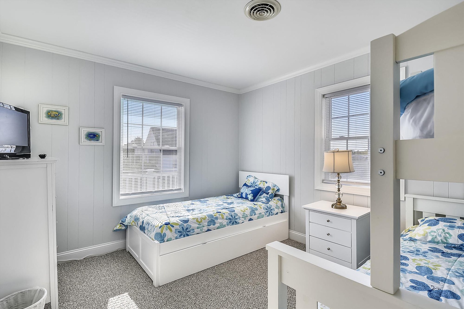 Drift off to sleep in this bright, coastal bedroom with twin beds dressed in cheerful floral linens. Natural light fills the space through large windows, creating a serene retreat for restful nights.