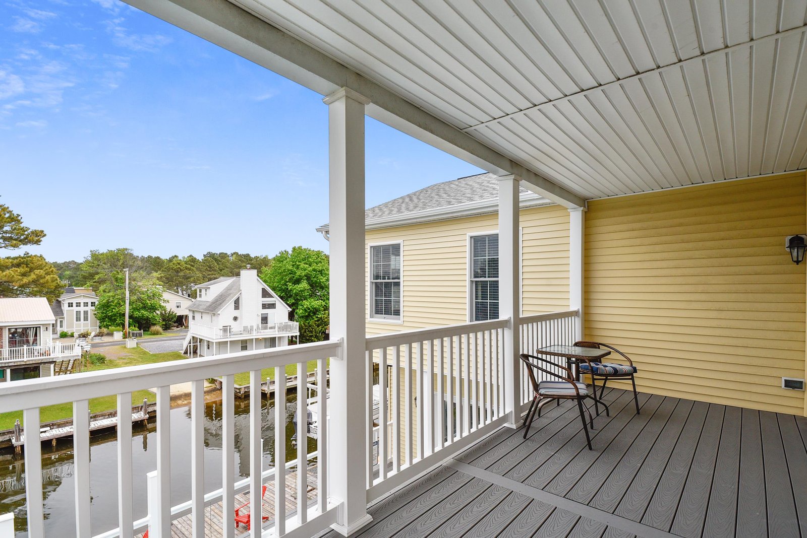 Covered balcony overlooking a peaceful waterfront neighborhood, with charming homes nestled among lush greenery along the quiet canal below.