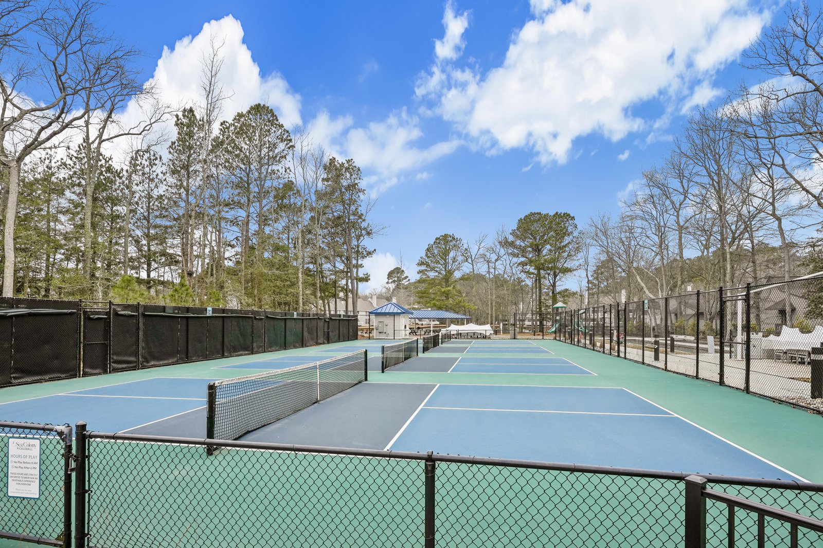 Well-maintained tennis courts surrounded by towering trees offer the perfect setting for an active vacation, with bright blue skies overhead and adjacent courts providing plenty of play options.