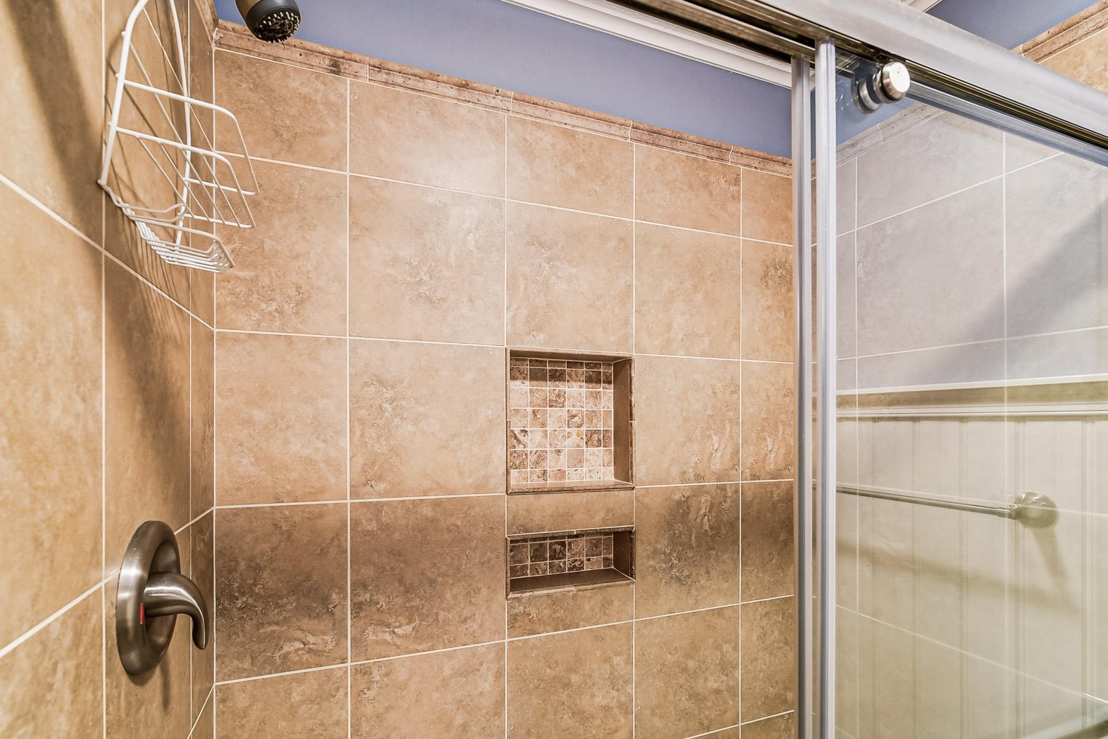 Step into your beautifully tiled walk-in shower with elegant earth-toned finishes, a rainfall showerhead, and convenient built-in storage niches for your essentials.