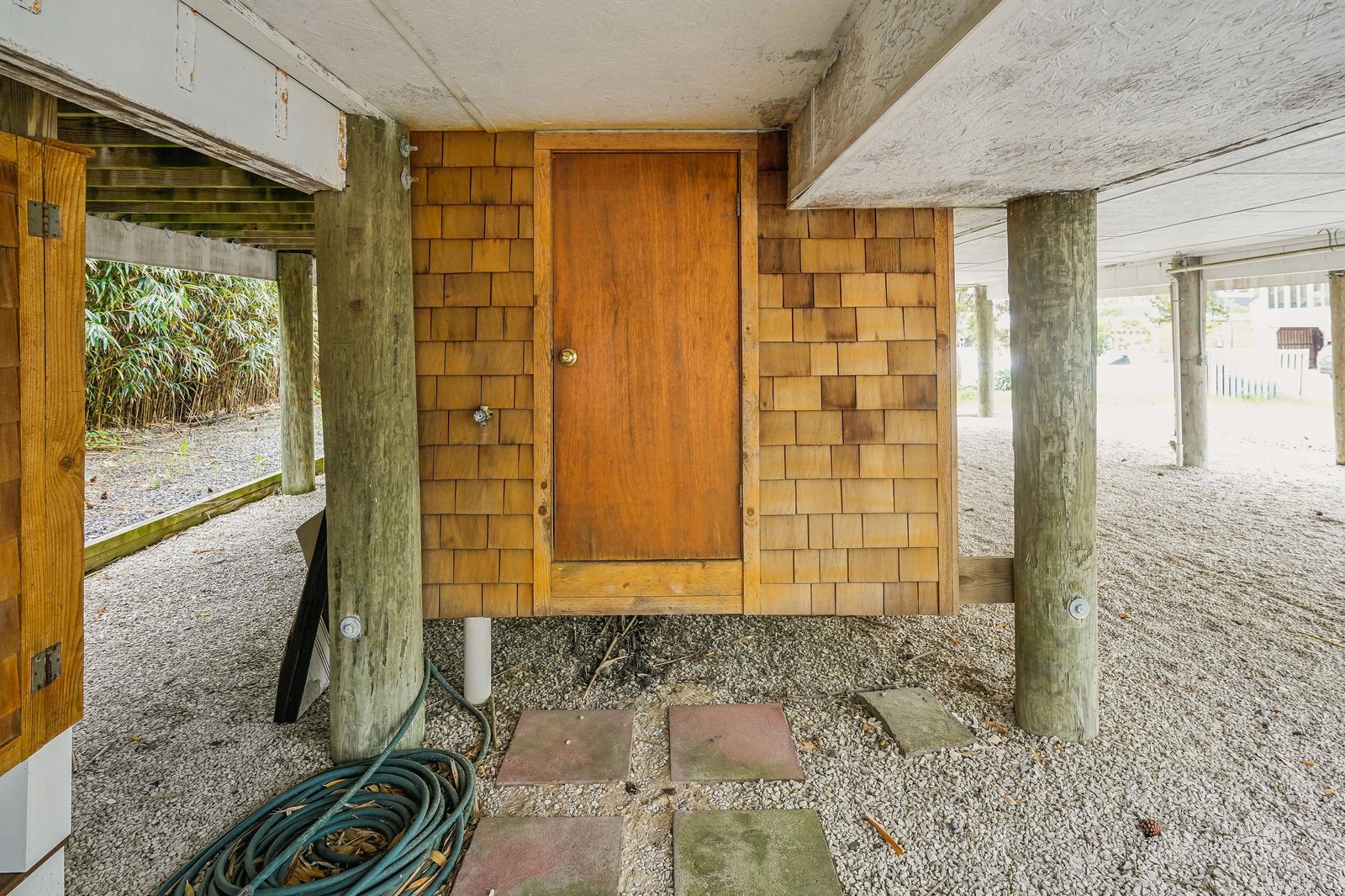 The property's covered entry sits on a gravel foundation with a central wooden door and cedar shake siding, offering covered parking space and outdoor access to surrounding natural greenery.