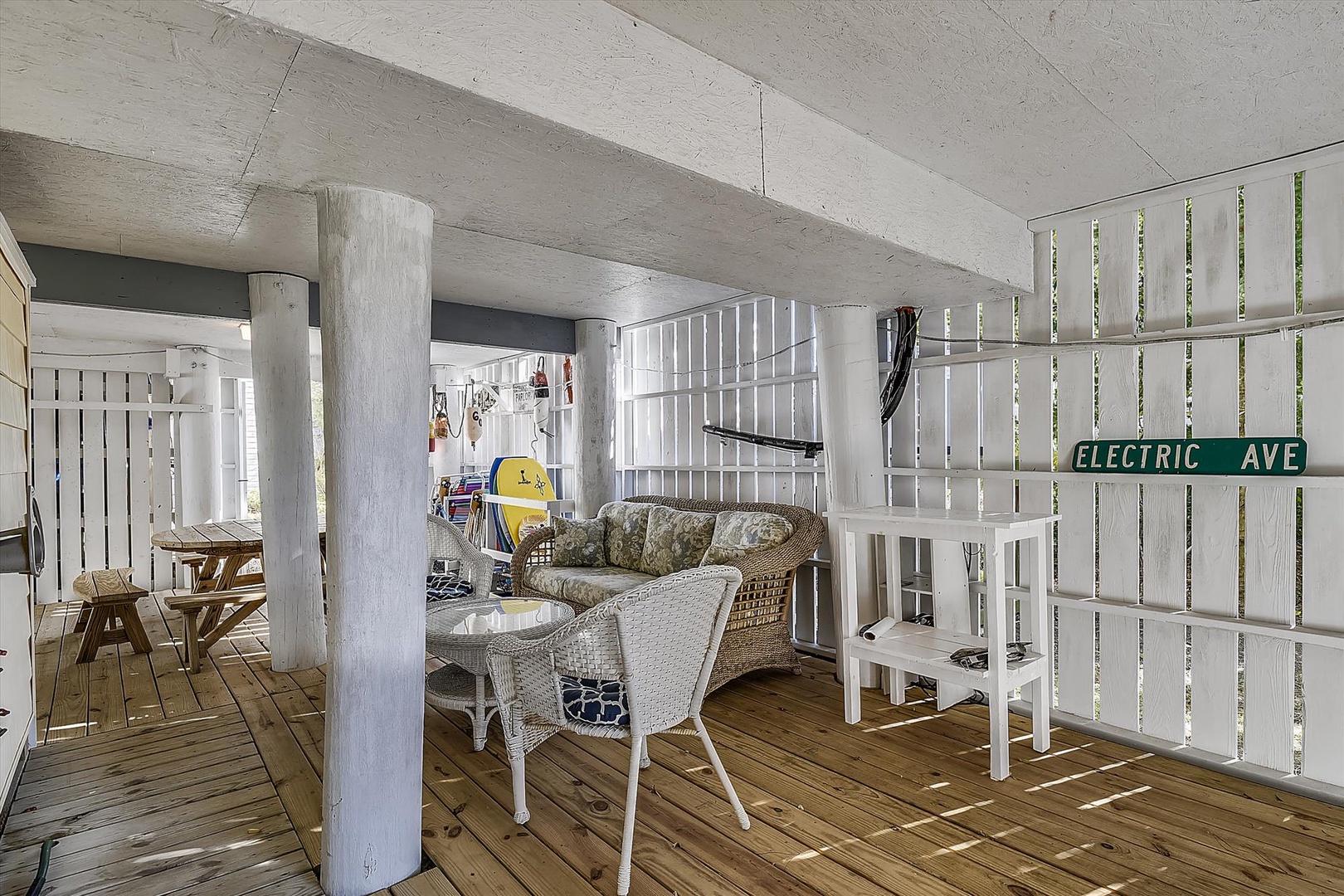 Unwind in your covered outdoor living space with cozy seating, perfect for morning coffee or evening relaxation under the shelter of this beachy-cool retreat.