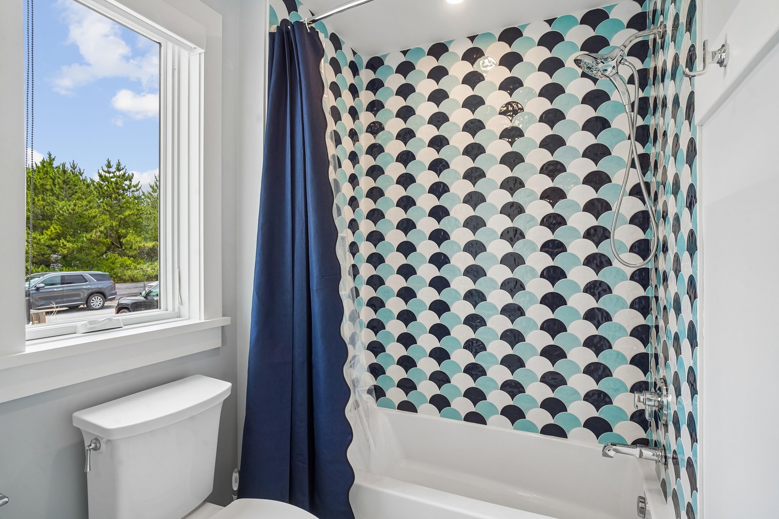 Freshen up in your stylish bathroom featuring a full tub and shower combo. The playful scalloped tile adds charm, while natural light brightens your routine.