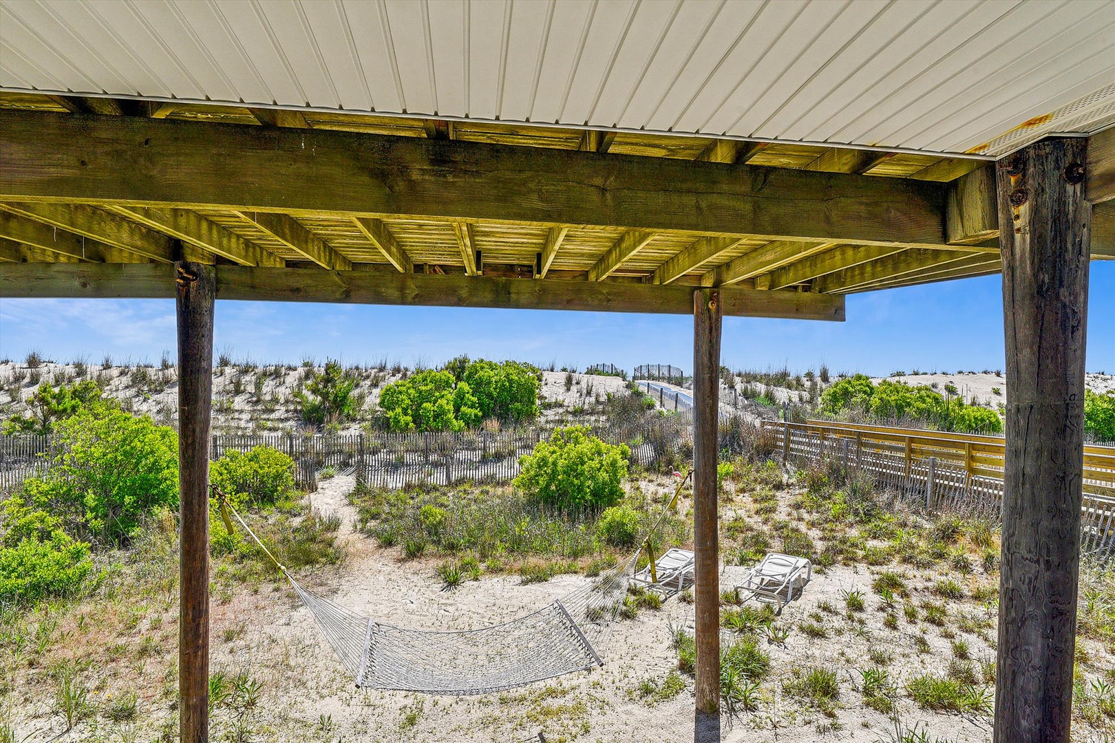 A covered porch overlooks coastal dunes and native vegetation, with lounge chairs and a hammock positioned just steps from the sand and sea.