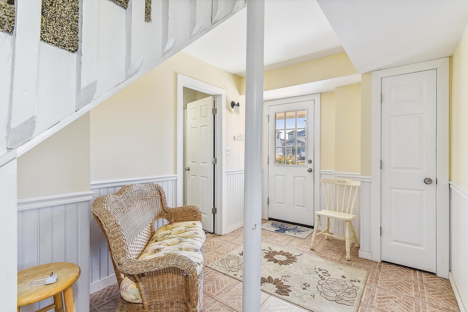 Welcome to your cozy entry, where soft yellow walls and a charming wicker chair invite you to settle in and feel at home from the moment you arrive.