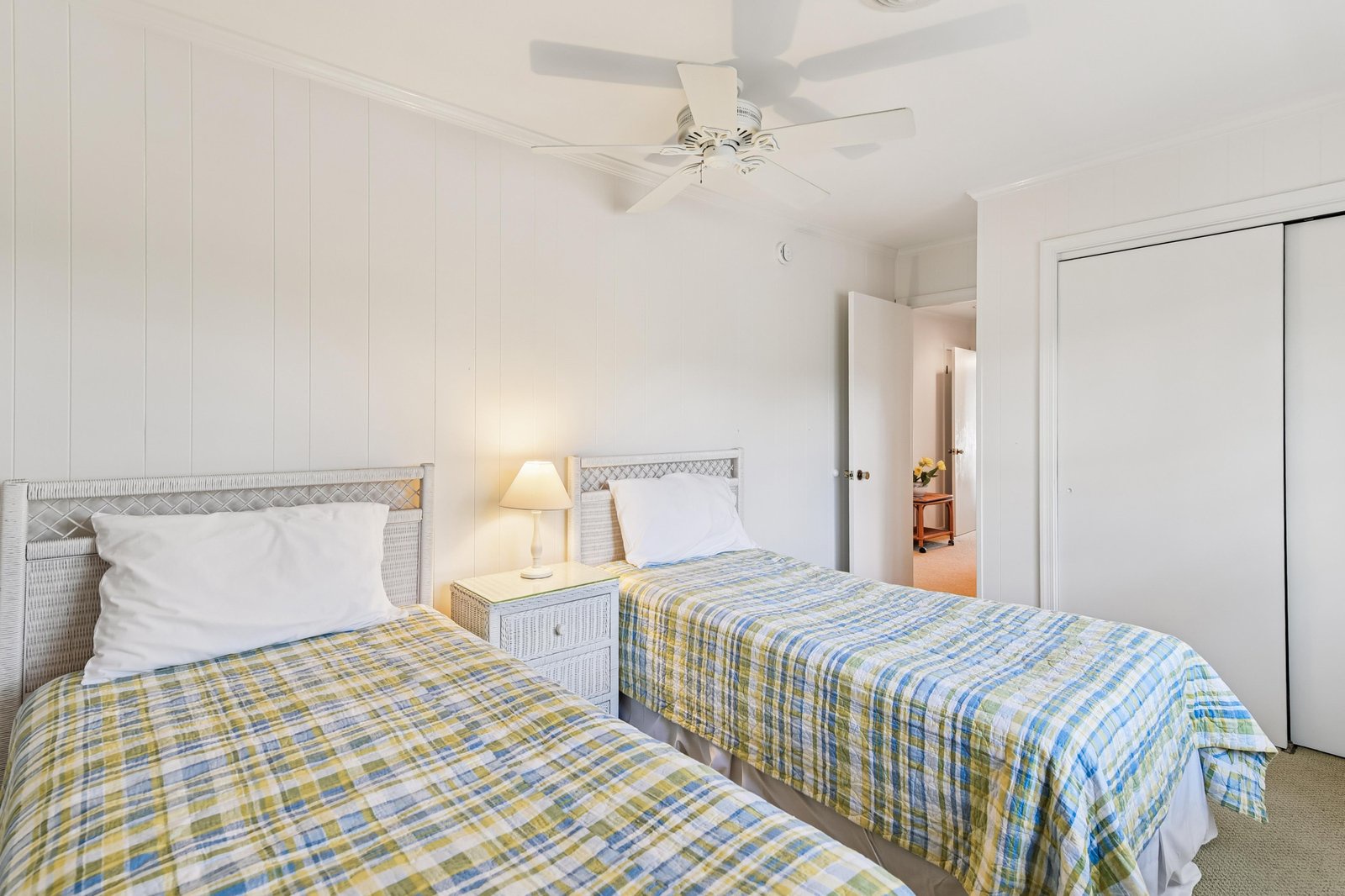 Two cozy twin beds await, dressed in cheerful plaid and bathed in gentle lamplight. The ceiling fan keeps you cool while crisp white walls create your peaceful retreat.