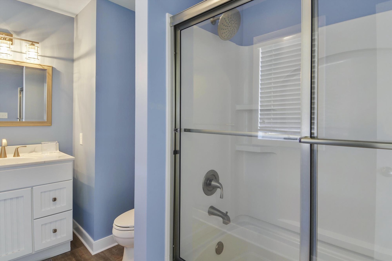 Step into your private bathroom retreat with a soothing blue-and-white palette. The walk-in shower features a sleek glass enclosure and convenient tub-shower combo, while soft natural light filters through the window.