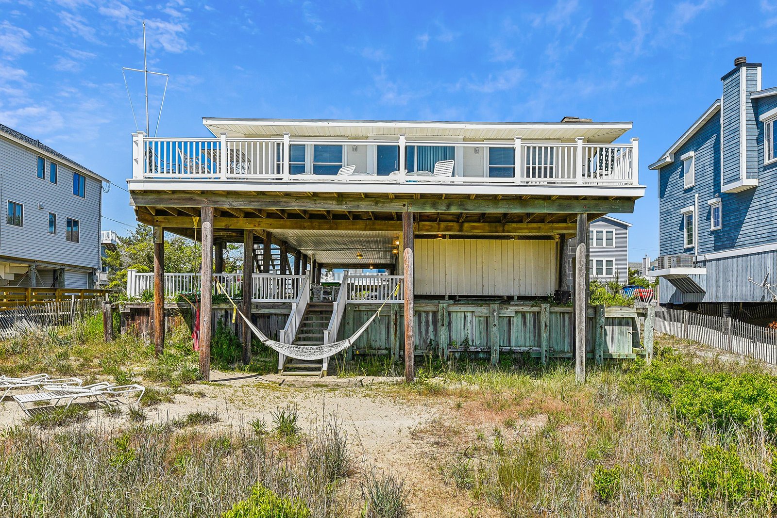 Beachfront property featuring elevated construction with expansive upper and lower deck spaces, direct beach access through native dune vegetation, and a hammock for relaxing between shore adventures.