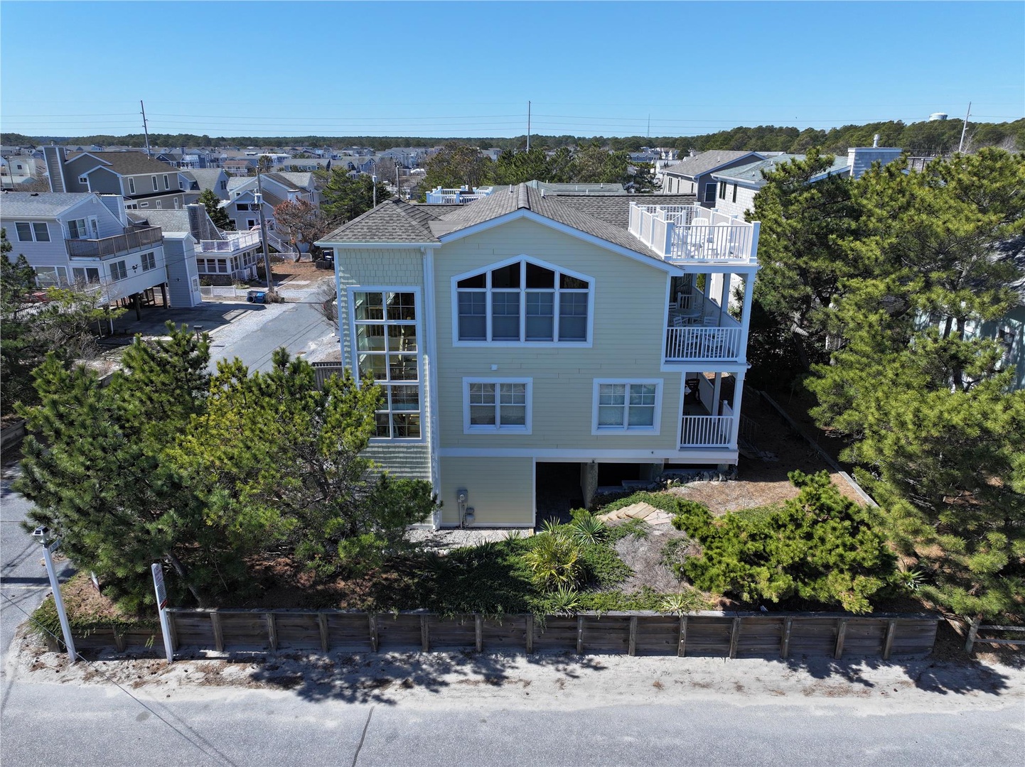 Elevated beach house with multiple balconies nestled in a quiet coastal neighborhood, surrounded by mature trees and neighboring homes.