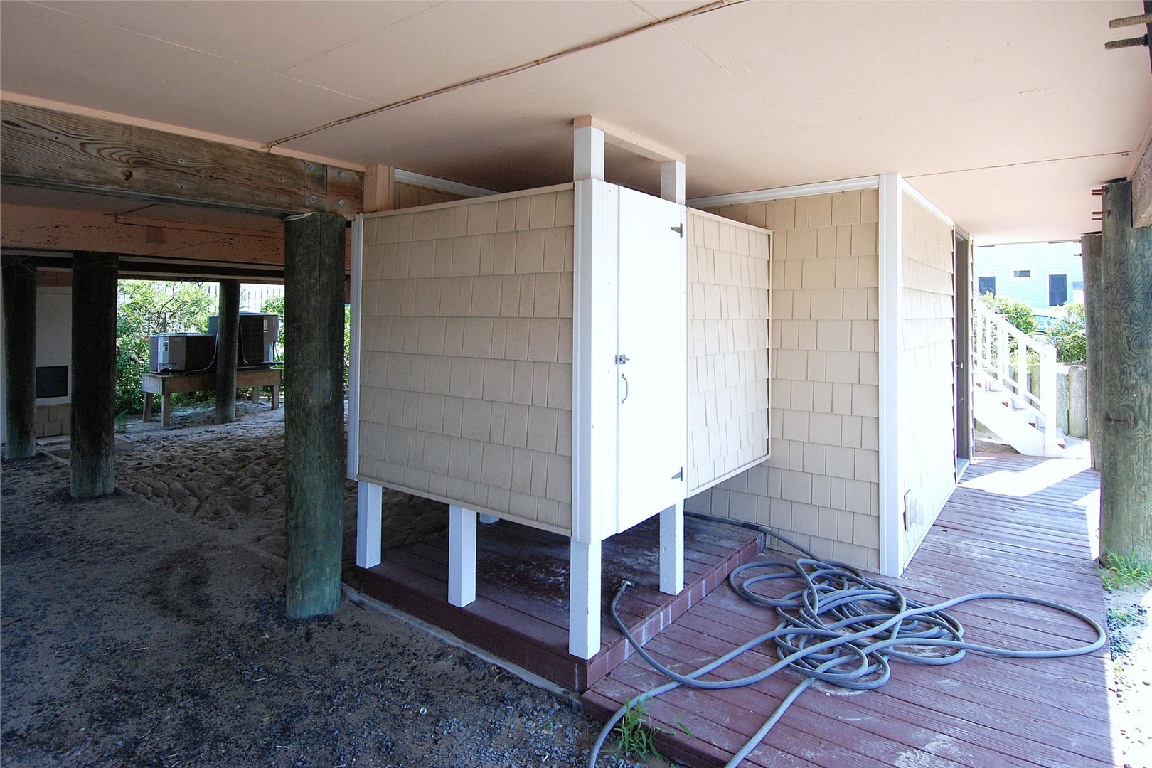 A waterfront property features outdoor shower facilities on a covered deck area with direct beach access, perfect for rinsing off after enjoying the sandy shores.