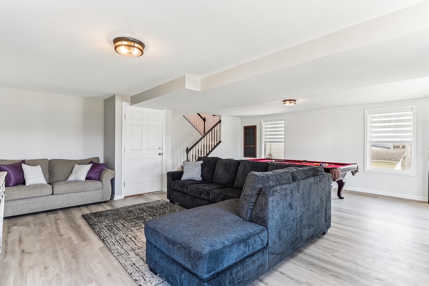 Unwind in this spacious upstairs lounge with plush seating, pool table entertainment, and bright natural light streaming through large windows.