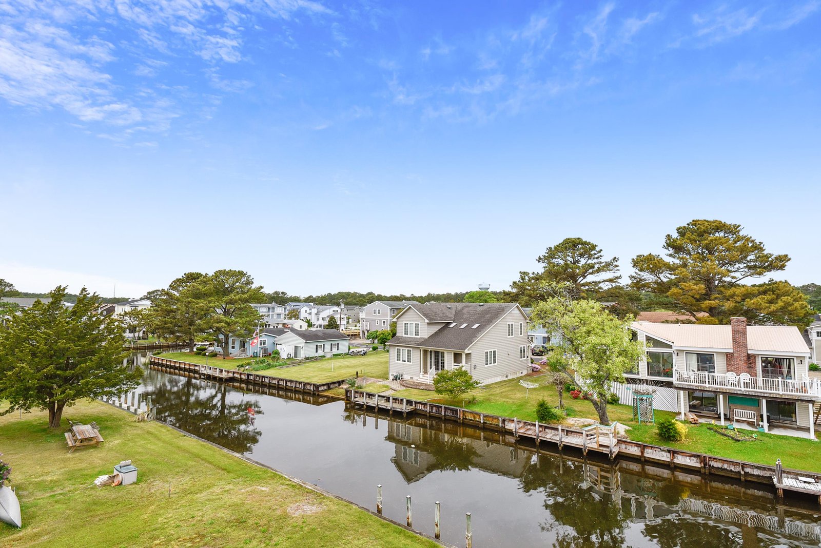 Peaceful waterfront community with private docks and manicured lawns under a bright coastal sky, offering direct access to serene canal waters.