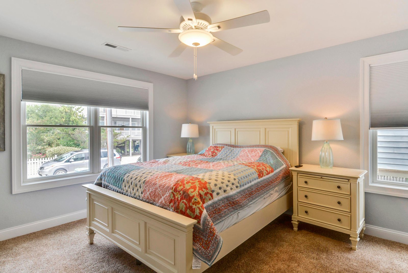 Your tranquil bedroom retreat features a plush bed with soft linens, flanked by warm bedside lamps. The ceiling fan keeps you comfortable while gentle natural light filters through the windows.