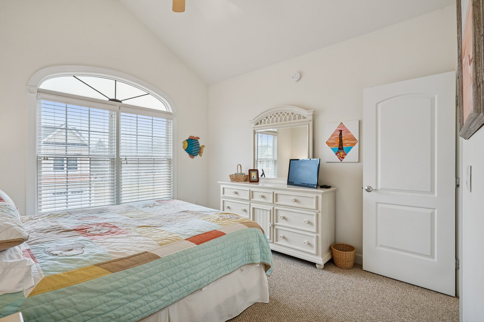 Unwind in your bright bedroom featuring an arched window, comfortable bed with colorful quilt, and coastal charm throughout.