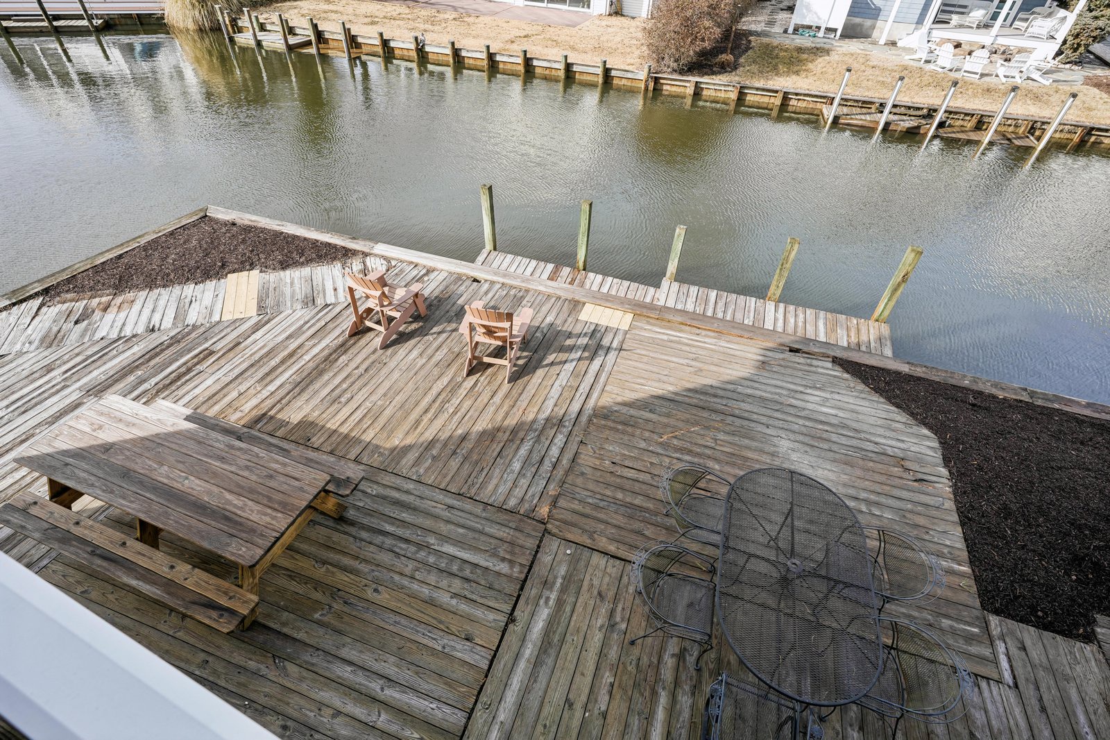 This waterfront property features a private dock and deck overlooking a calm inlet, offering peaceful outdoor seating surrounded by natural waterways and nearby properties.