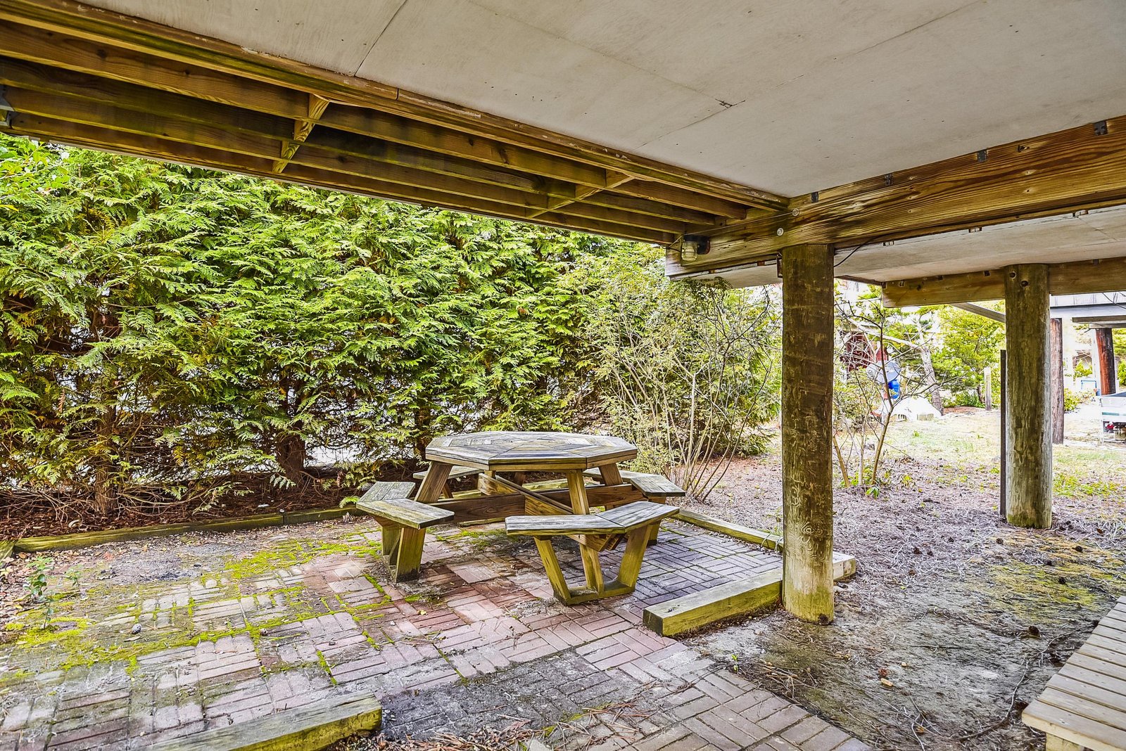 A sheltered outdoor space featuring a wooden picnic table surrounded by lush greenery, perfect for enjoying meals or relaxing outside.