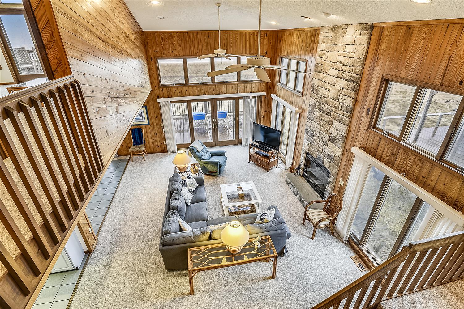 Soaring ceilings and walls of windows fill this bright, open living space with natural light, inviting you to relax by the striking stone fireplace.