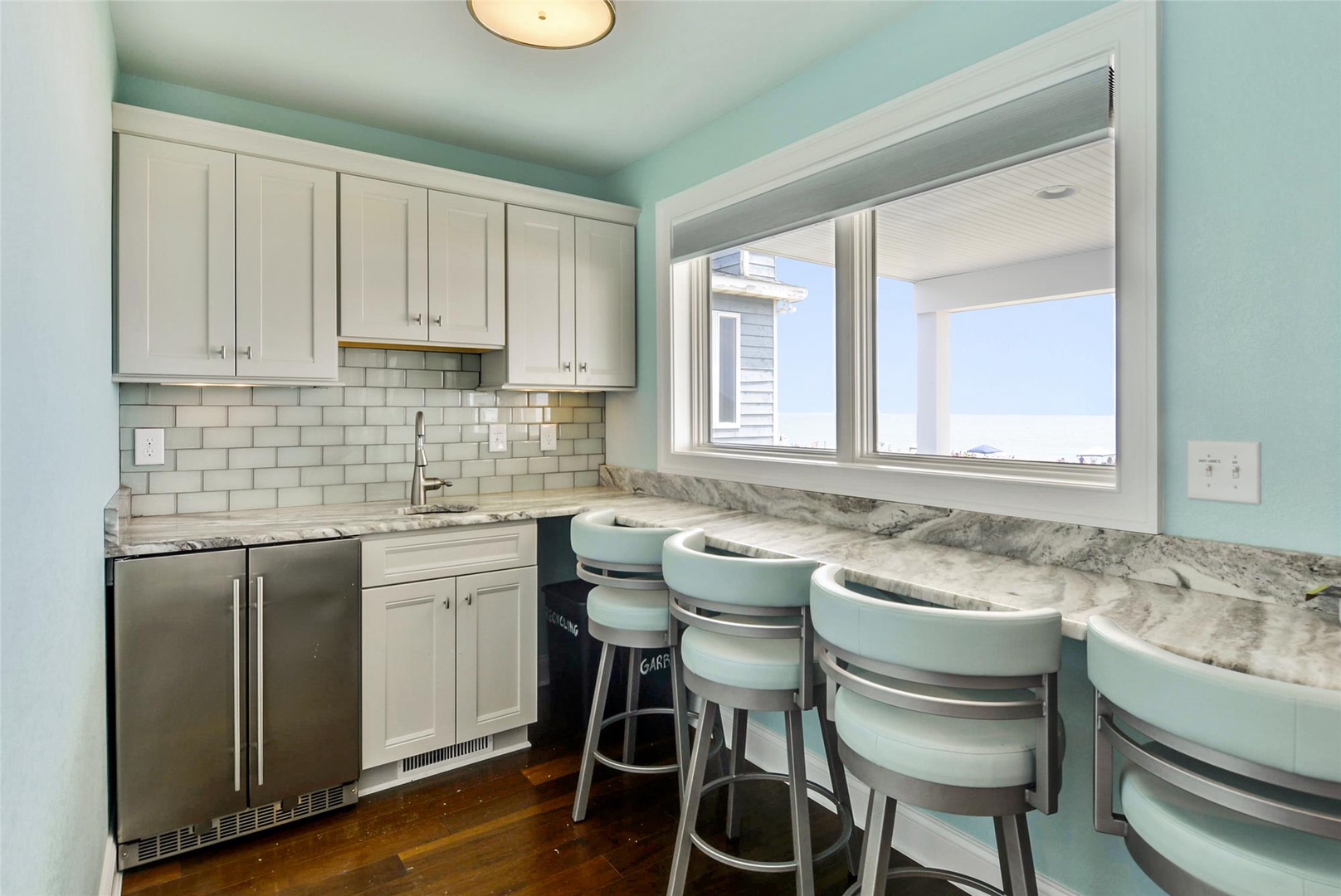 Gather at the marble bar with ocean views framed by the window, where coastal breezes meet modern convenience in your fully-equipped kitchen space.
