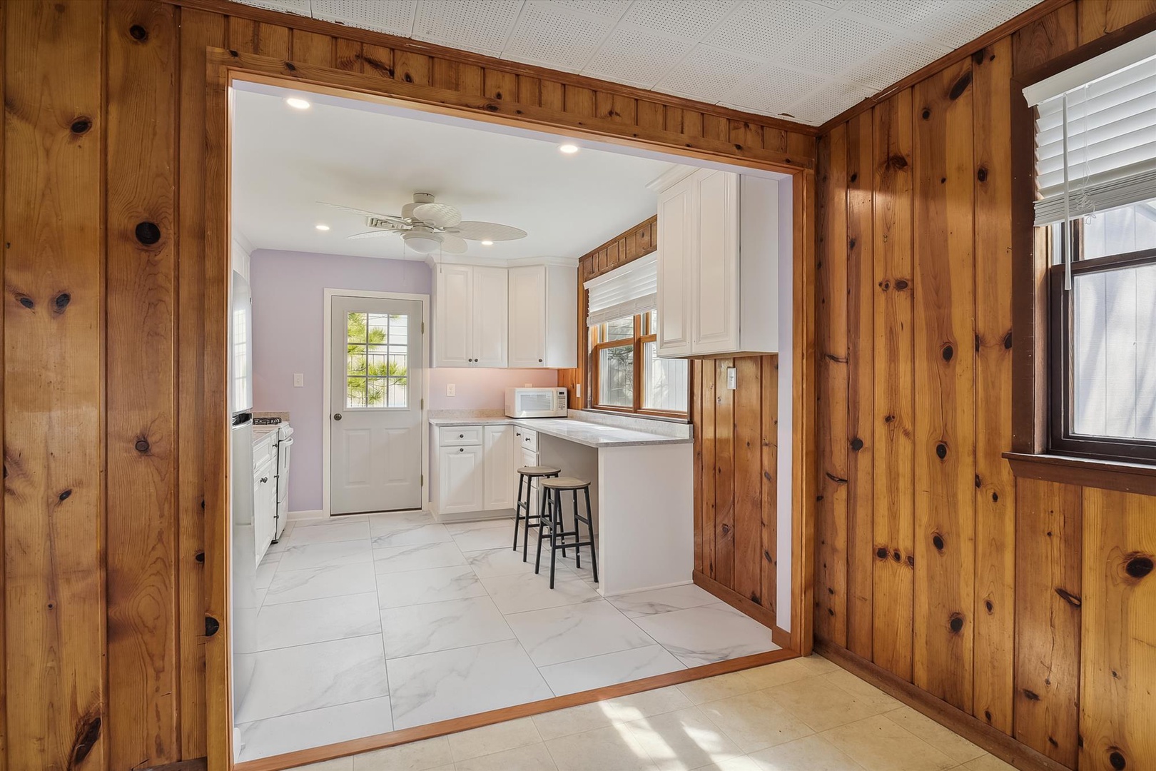 Rustic knotty pine walls frame your modern kitchen with crisp white cabinetry, marble countertops, and cozy breakfast bar—a bright, inviting space where you'll love whipping up your morning coffee.